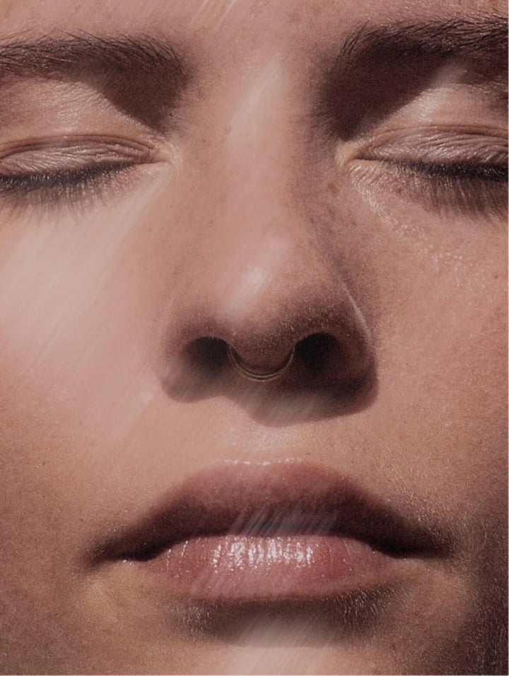 Close-up of a serene face with closed eyes, showcasing smooth skin and a subtle nose ring.